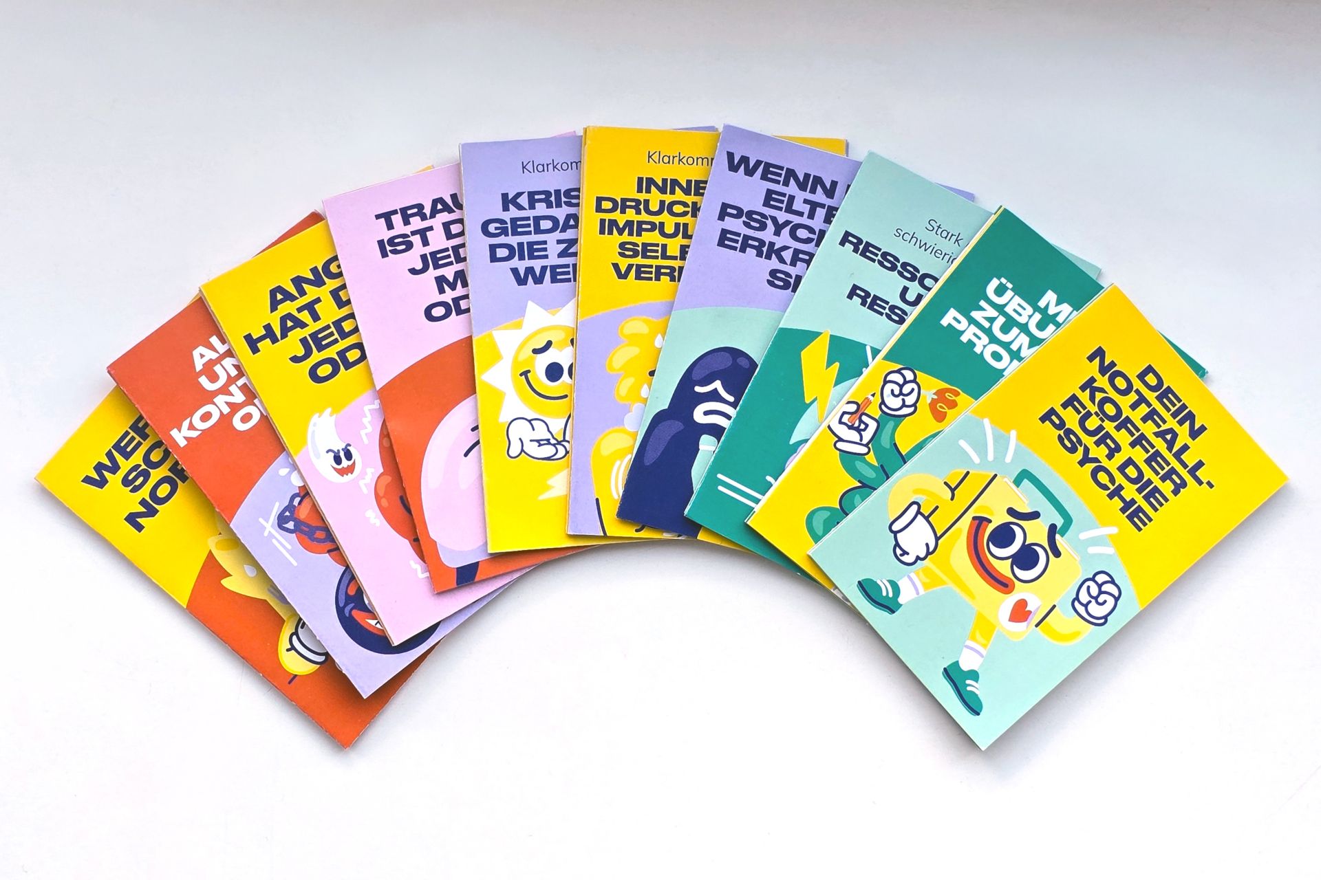 Die neu gestalteten Info-Pocket-Guides von Irrsinnig Menschlich e.V. liegen aufgefächert nebeneinander; die zehn verschiedenen Titel rund um psychische Gesundheit sind sichtbar.